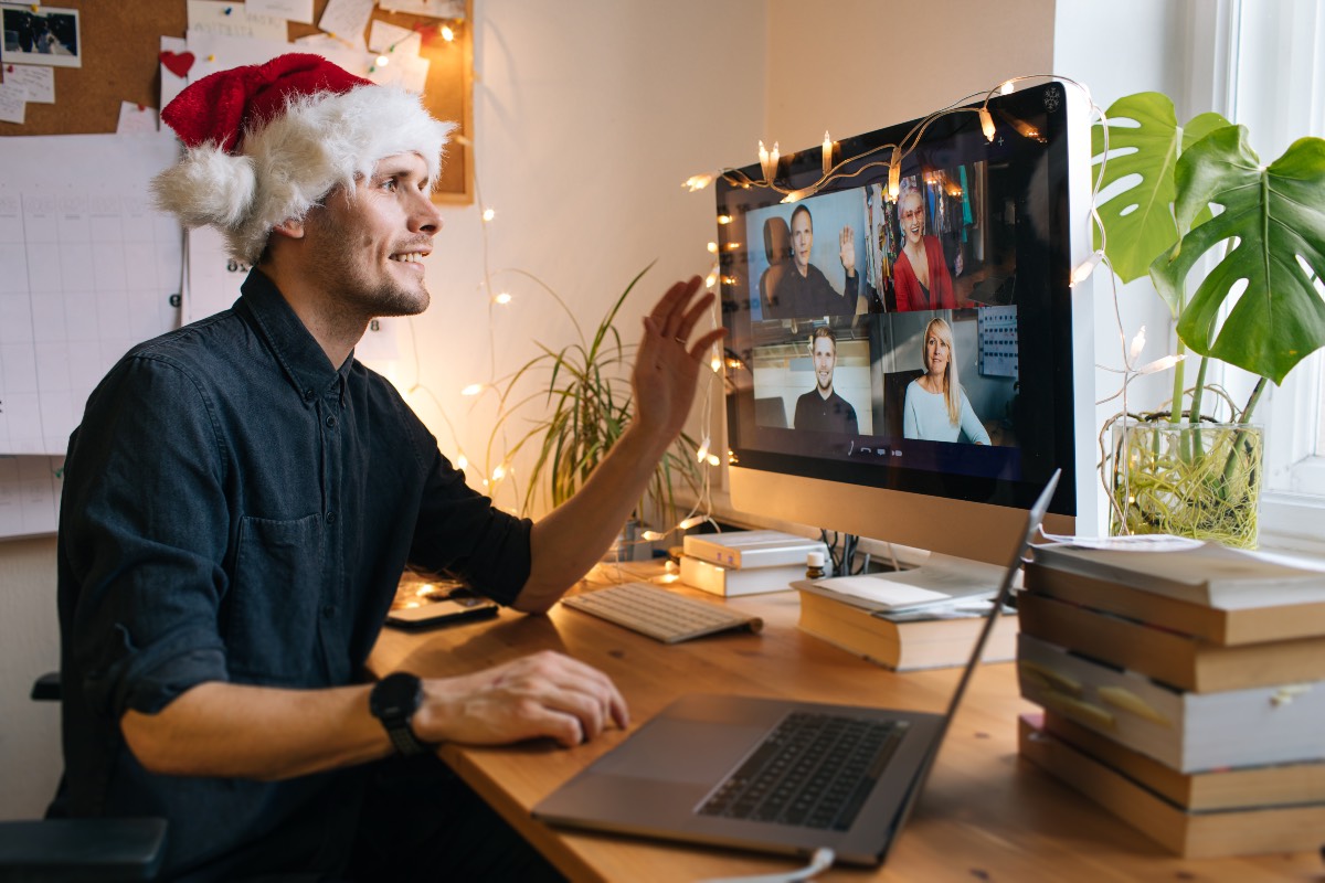 Homme avec un bonnet de Noël en télétravail faisant une fête virtuelle avec ses collègues